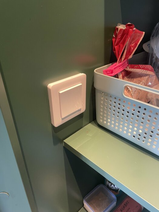 Vägg med ljusbrytare, hylla med korg, påsar och lådor, heminredning.