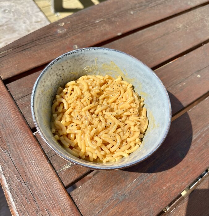 Skål med nudlar på träbord utomhus. Soligt väder. Sannolikt snabbmat eller enkel måltid.