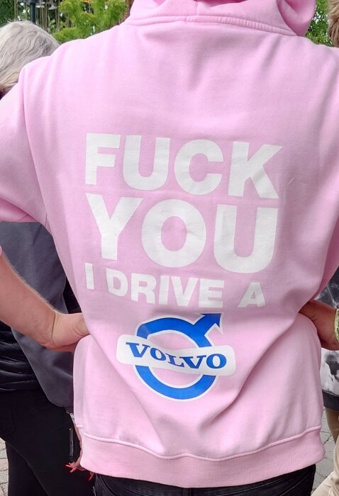 Person bär rosa hoodie med tryck: "F**K YOU I DRIVE A VOLVO". Utescen, dagsljus. Provokativt budskap.