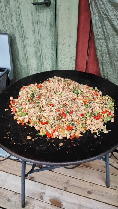 En stor paellapanna med matlagning av wokade nudlar och blandade grönsaker utomhus.