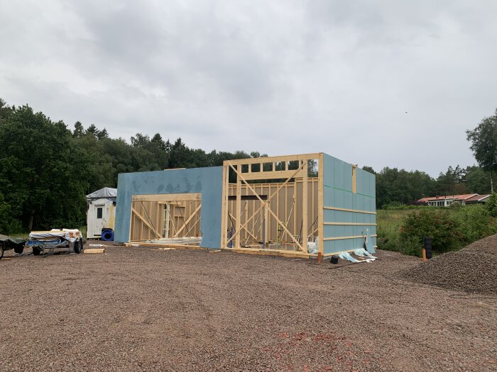 Byggplats med trästomme och isolermaterial, grushög, skogsbakgrund, mulet väder, under konstruktion hus.