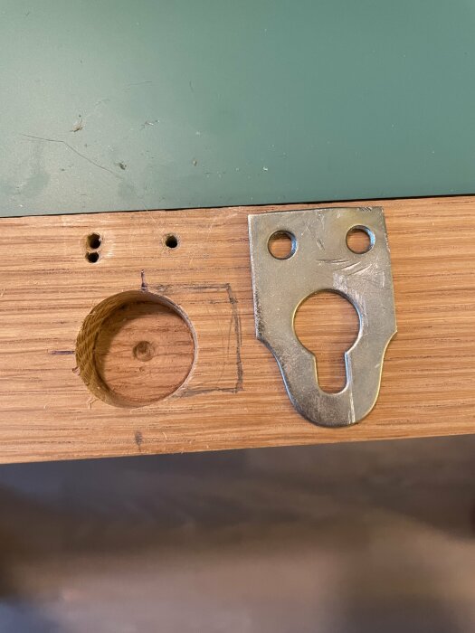 Urtagen cirkel i trä, metallplåtdel bredvid, möjlig dörrkomponent, skruvhål, slitet, arbetsyta.