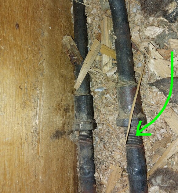 En kabel ligger längs ett trägolv med spånskräp; en grön pil pekar på kopplingen.