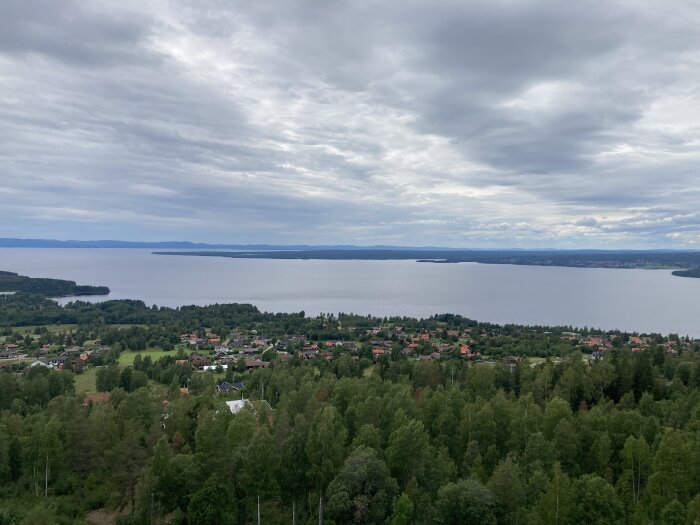 En vidsträckt utsikt över en sjö med skog och bebyggelse under en molnig himmel.