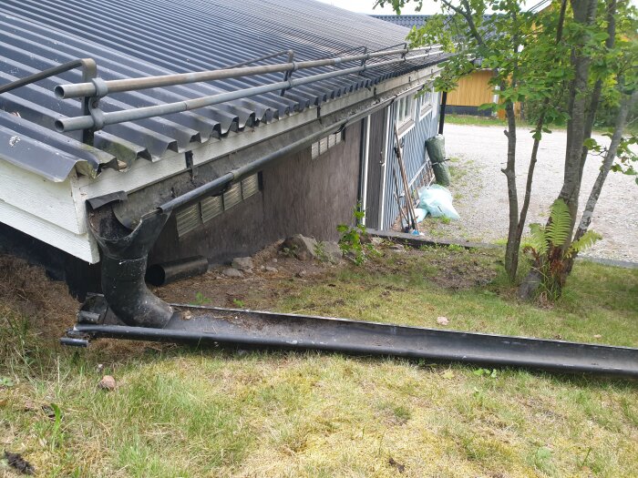 Nedstörtad takränna vid hus, skadat tak och stuprör på marken, disig dag.