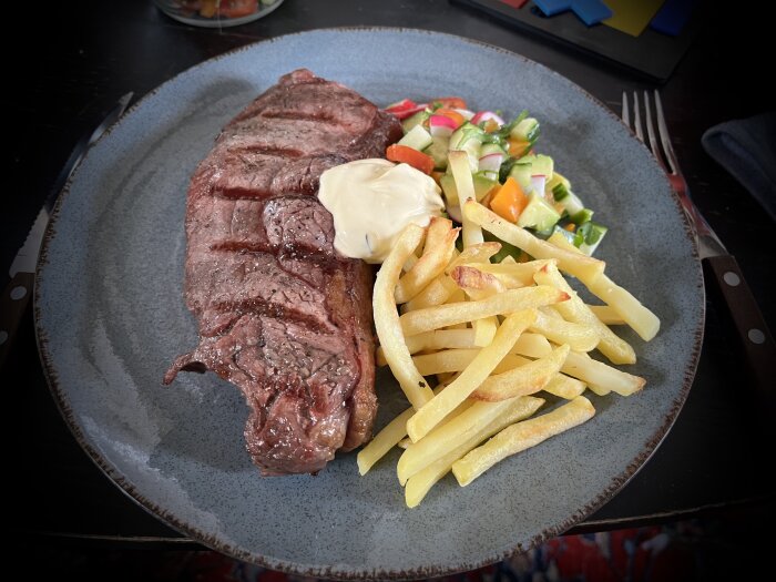 Ett välstekt entrecôte med pommes frites, bearnaisesås och fräsch grönsallad serveras på keramiktallrik.