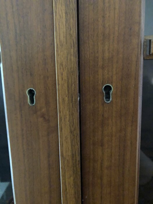 Två träskåpsdörrar nära stängda, med synliga nyckelhål, mörkbrunt trä, inomhusmiljö.