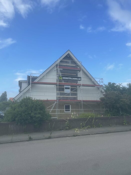 Ett hus med vit och röd byggnadsställning, blå himmel, träd och en staket.