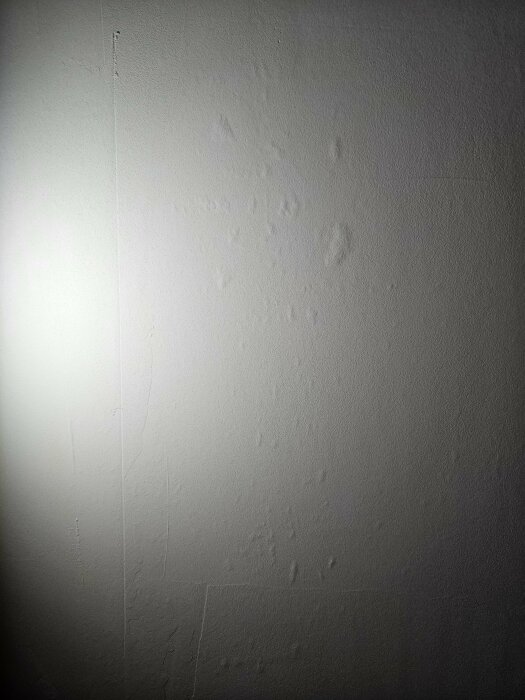 En vit vägg med fläckar och revor, upplyst i ena hörnet.