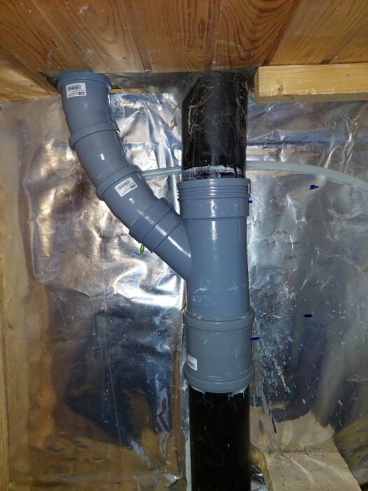 PVC-rörinstallation genom isolering i en grov väggkonstruktion, sannolikt avlopp eller ventilation.