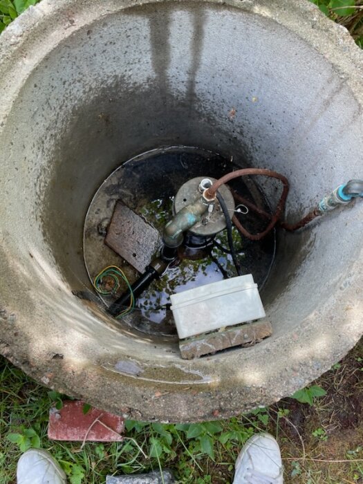 Brunn med pump och rör, nedsänkt elektronik, tegelstenar, vattensamling, skor vid kanten.