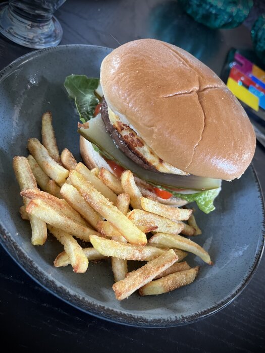 Hamburgare med pommes frites på en grå tallrik. Maten ser aptitretande ut, serverad och redo att ätas.