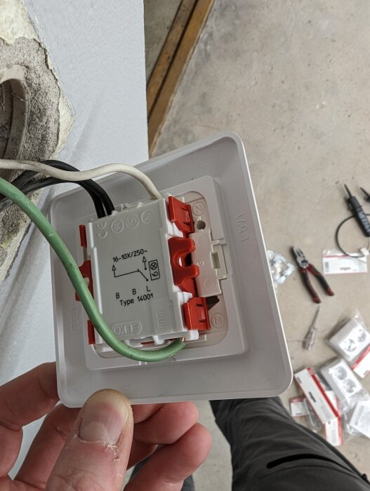 Installation av eluttag. Vit vägg, arm i förgrunden, elektriskt material synligt, oavslutat arbete.