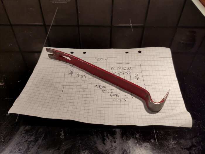 Röd bågfil ligger på rutigt papper med matematiska beräkningar, på en mörk yta.