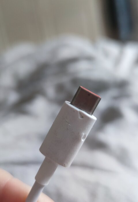 USB-C-kabel närbild, använd och smutsig, otydlig bakgrund med mönstrat tyg.