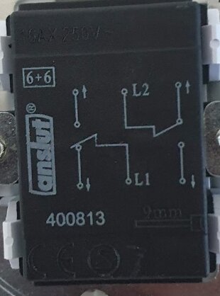 Svart elektriskt relä med kopplingsschema, märkningar och fästskruvar, mot vit bakgrund.