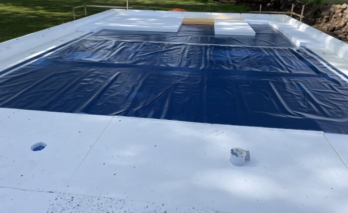 Swimming pool covered with blue tarp, surrounded by white deck, trees and grass visible.