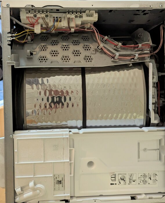 Insidan av en demonterad torktumlare med synliga elektriska kopplingar, slangar och komponenter.