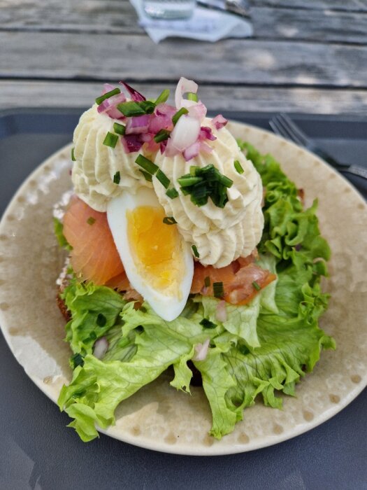 En smörgås med lax, ägg, majonnäs och grön sallad på en beige tallrik.