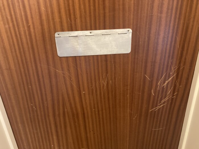 Brun dörr med tom namnskyltplats och repor på ytan.