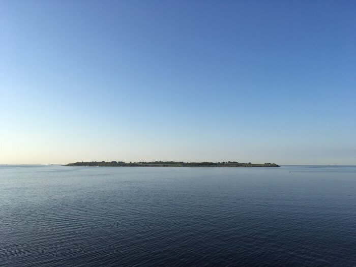 Klart väder, lugnt hav, horisontlinje, liten ö, lugn, blå himmel, inga moln, fridfullt landskap.