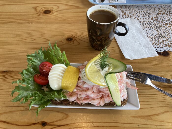 Räkmacka med citron och dill, kaffe, på träbord vid spetsduk.