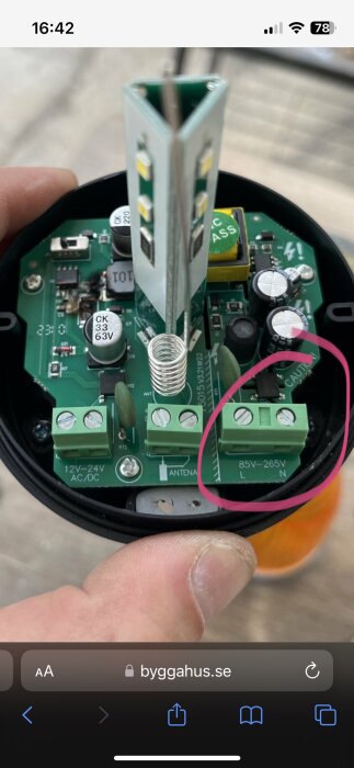 Öppnad elektronisk anordning med kretskort, kondensatorer, och fjädrar—i handen med oskarp bakgrund.