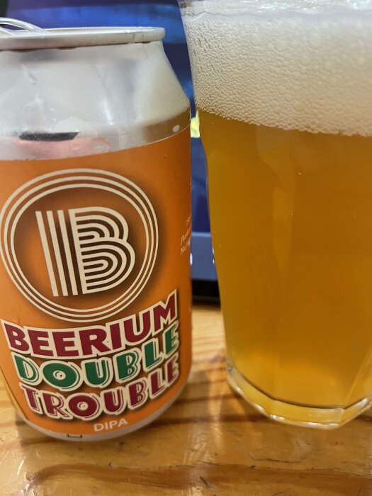 En ölburk med texten "BEERIUM DOUBLE TROUBLE DIPA" och ett halvfullt glas med öl och skum.