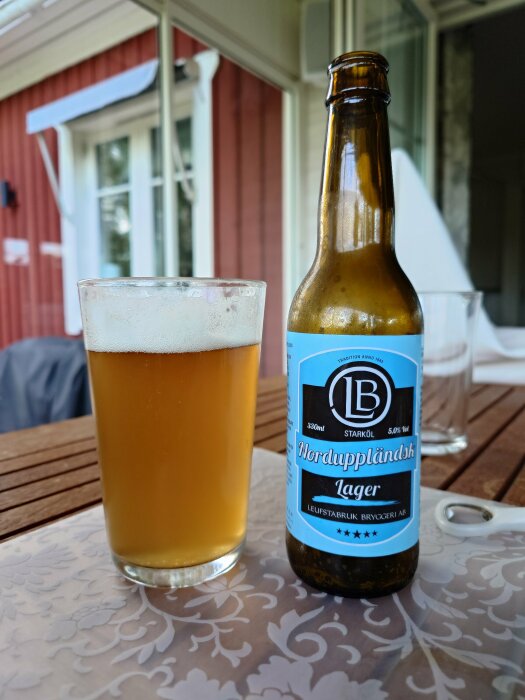 Ölflaska och glas på träbord, veranda, sommartid, duk med mönster, Norduppländsk Lager, avkoppling.