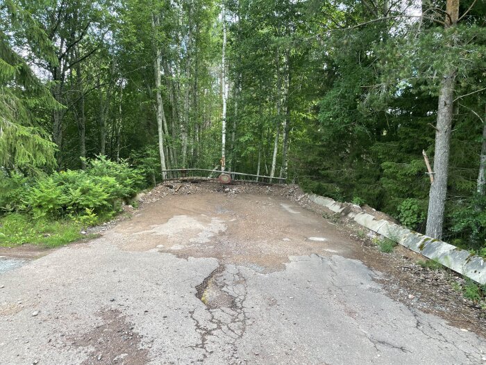 En avspärrad och förfallen väg leder in i en grön lövskog; ingen trafik tillåten, försummelse och natur.