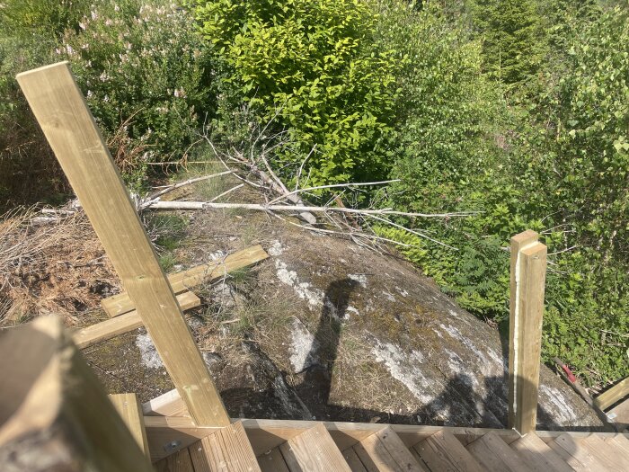 Puiset kaiteet terassilla, etäisyys on 159 cm. Taustalla näkyy kiveä ja vehreää kasvillisuutta.