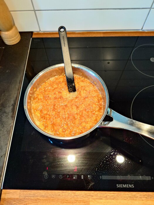 Kastrull med maträtt på induktionshäll, träredskap, köksmiljö, Siemens spis, matlagning, gryta med slev.