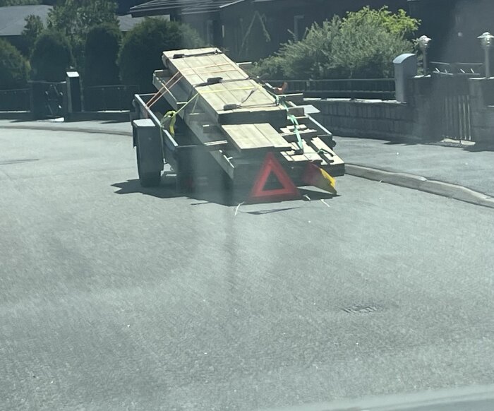 Släpvagn med bräder och varningstriangel på en solig väg.