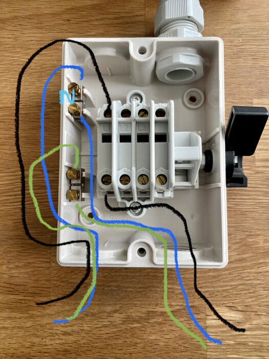 Öppen elektrisk anslutningsdosa med märkta kablar och terminaler på träunderlag.