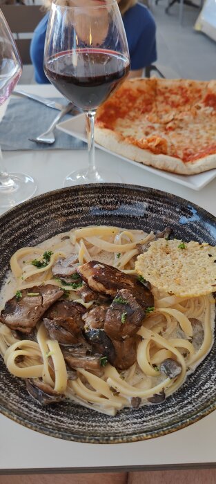 Pasta med svamp och kött, parmesanchips, pizza i bakgrunden, vin, restaurangmiljö, lunch eller middag.