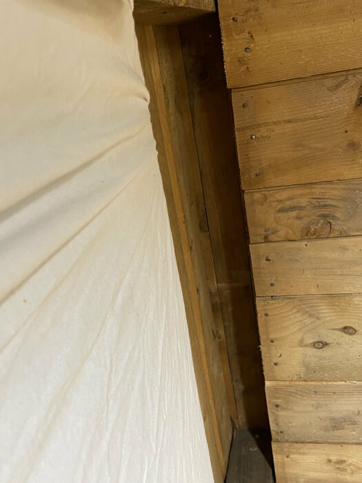 Hörn med träpanel och vit vägg, möjligen inomhus, skuggrigt, spår av konstruktion eller renovering.