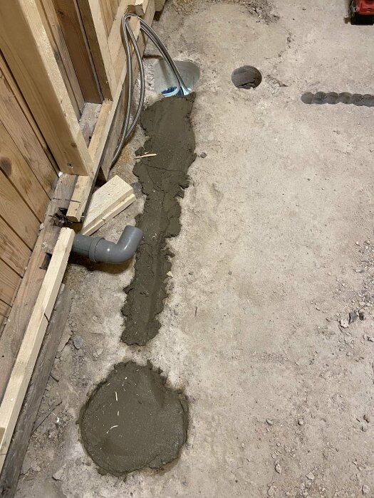 Nygrävd ränna i betonggolv med avloppsrör och nylagt, vått cement. Arbetsplats i förberedelse för installation.