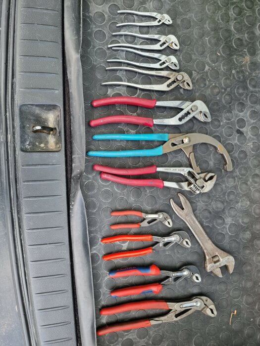 Uppsättning verktyg, inklusive tänger och skiftnycklar, ordnade på en bilgolvmatta.