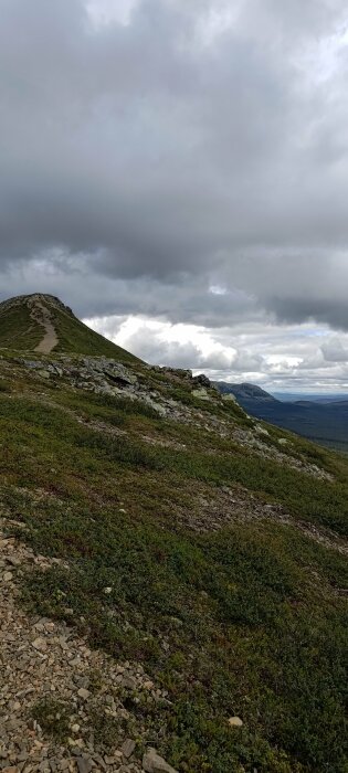 Bergstopp, kargt landskap, molnig himmel, vandringsled, ingen synlig mänsklig aktivitet, potential för dåligt väder, nordiskt eller alpint utseende.