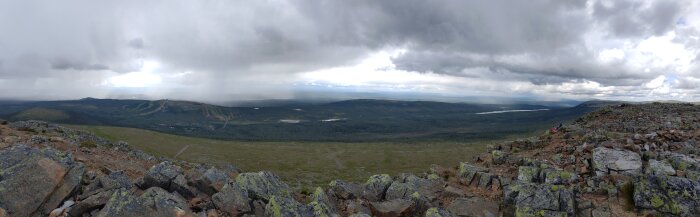 Panoramavy över karg fjällterräng med molntäcke, några vandrare i fjärran, vidsträckt utsikt, stillhet.