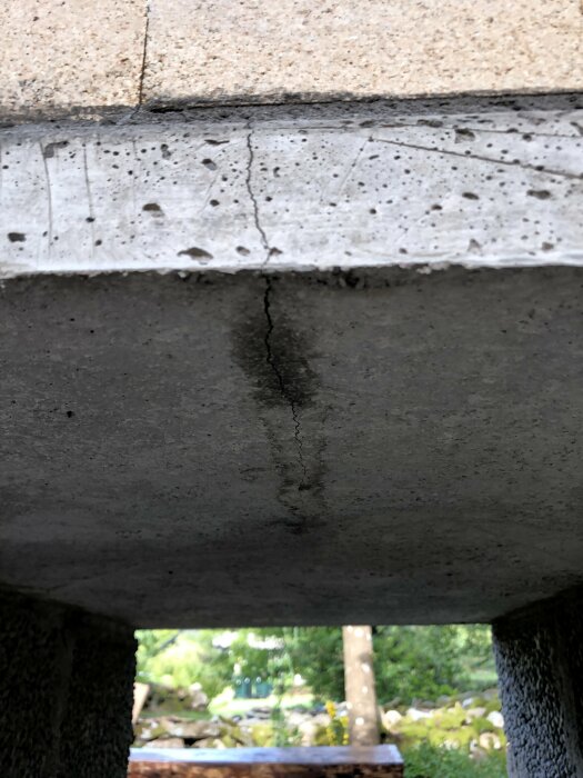 Betongstruktur med sprickor, sannolikt en bro eller ett viadukt, skadad, underifrån perspektiv, oskarpt bakgrundsljus.