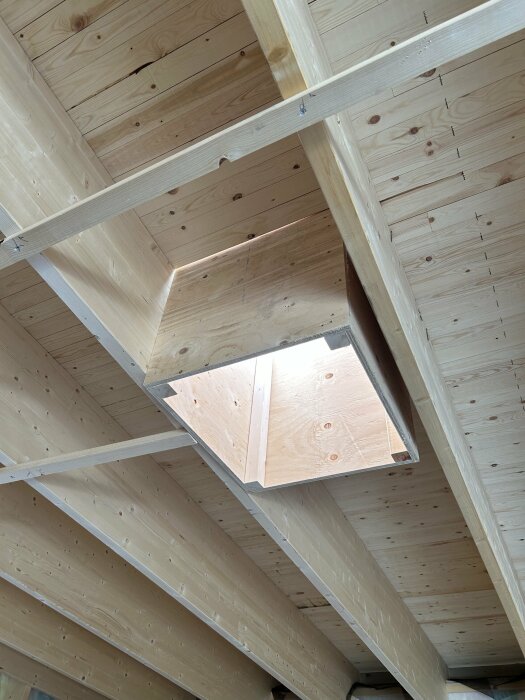 Träbjälklag och spånskiveplattor ur fågelperspektiv med en öppning som skapar en geometrisk kontrast.