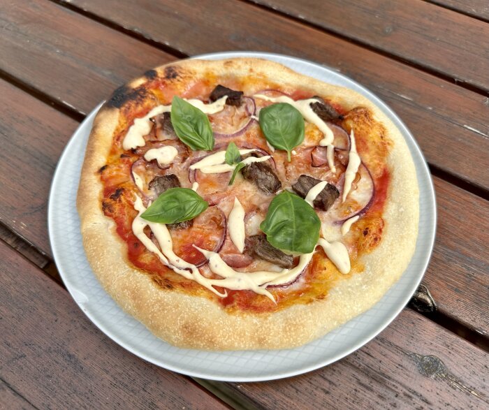 En pizza med tomatsås, ost, lök, champinjoner, kött, basilika på en träbord.
