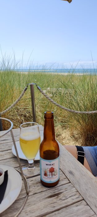 Strandvy, ölflaska, glas, repstaket, person, blå himmel, avkoppling.