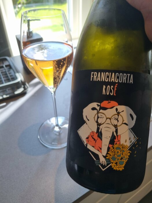 Flaska Franciacorta Rosé med vin i glas, etikett har elefantillustration, inomhus, dagtid.