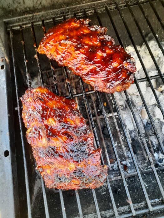 Två grillade revbensspjäll med glaserad yta över glödande kol.