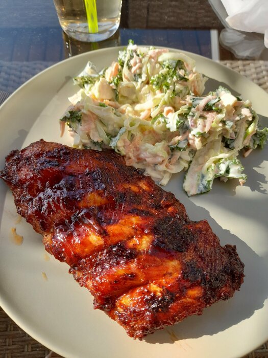 Ett fat med grillad revbensspjäll och cole slaw under solljus utomhus.