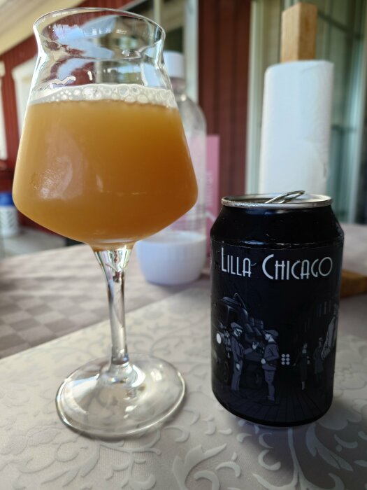 Ett grumligt, ljusgult öl i elegant glas bredvid en burk med texten "Lilla Chicago".