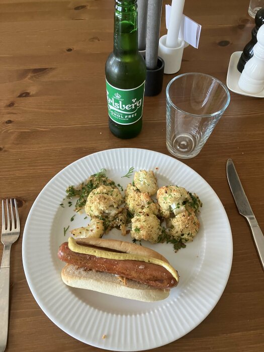 Måltid med korv, senap, blomkål, örtkrydda och alkoholfri öl från Carlsberg på bordet.