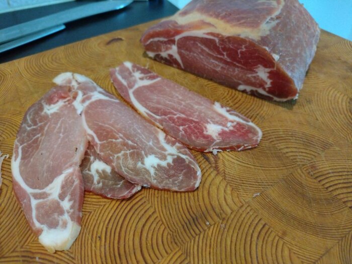 Skivad capicola och hela biten på träskärbräda, kniv i bakgrunden.